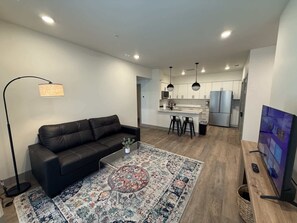 A modern living room with a black leather sofa, a coffee table, and a patterned rug. - [R17] 1BD/1BA Condo, Brand New, Furnished & Work-Ready! (Austin)