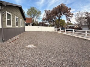 A gravel-covered outdoor area with a white fence, a building with windows, and trees in the background. - Your Home Away From Home
Quiet, Modern, & Open 1 (Delta)