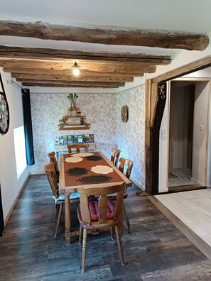 A dining area with a wooden table and chairs, a decorative wall, and a ceiling with exposed beams.