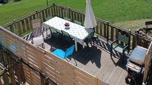Une terrasse avec une table et des chaises, offrant une vue sur un paysage verdoyant avec un village et des montagnes.