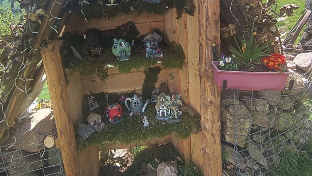 Une structure en bois, ornée de petites maisons et de figurines, entourée de verdure et de rochers.