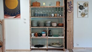 Une cuisine avec des étagères en bois, une fresque représentant un soleil, et une variété de plats et d’ustensiles de cuisine.
