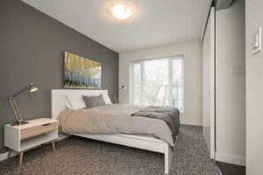 Une chambre à coucher avec un lit, une table de chevet, une lampe et une fenêtre.