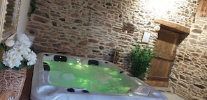 Un mur de pierres, une armoire en bois et un jacuzzi éclairé de lumières vertes.
