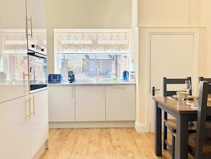 A kitchen with white cabinets, a window with a view of a brick building, a coffee maker, and a dining table with chairs. - Prime York City Centre Flat Near Station (York)