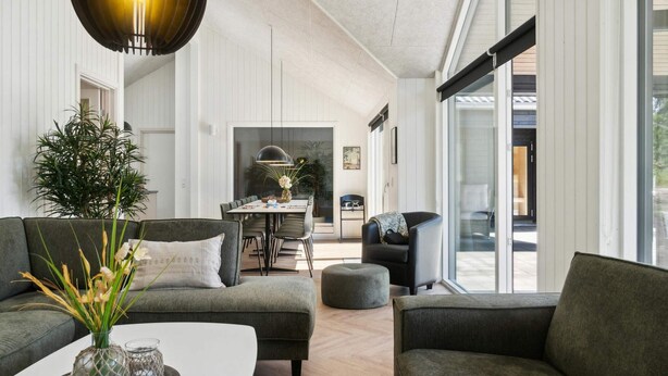 A modern living room with a sofa, ottoman, and a dining area with a table and chairs. - 5 Star Holiday Home in Hojby (Hojby)