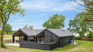 A modern black building with a sloped roof, large windows, and a patio area with outdoor seating. - 5 Star Holiday Home in Hojby (Hojby)