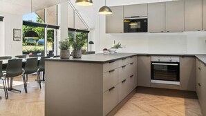 A modern kitchen with a central island, built-in appliances, and a dining area with chairs. - 5 Star Holiday Home in Hojby (Hojby)