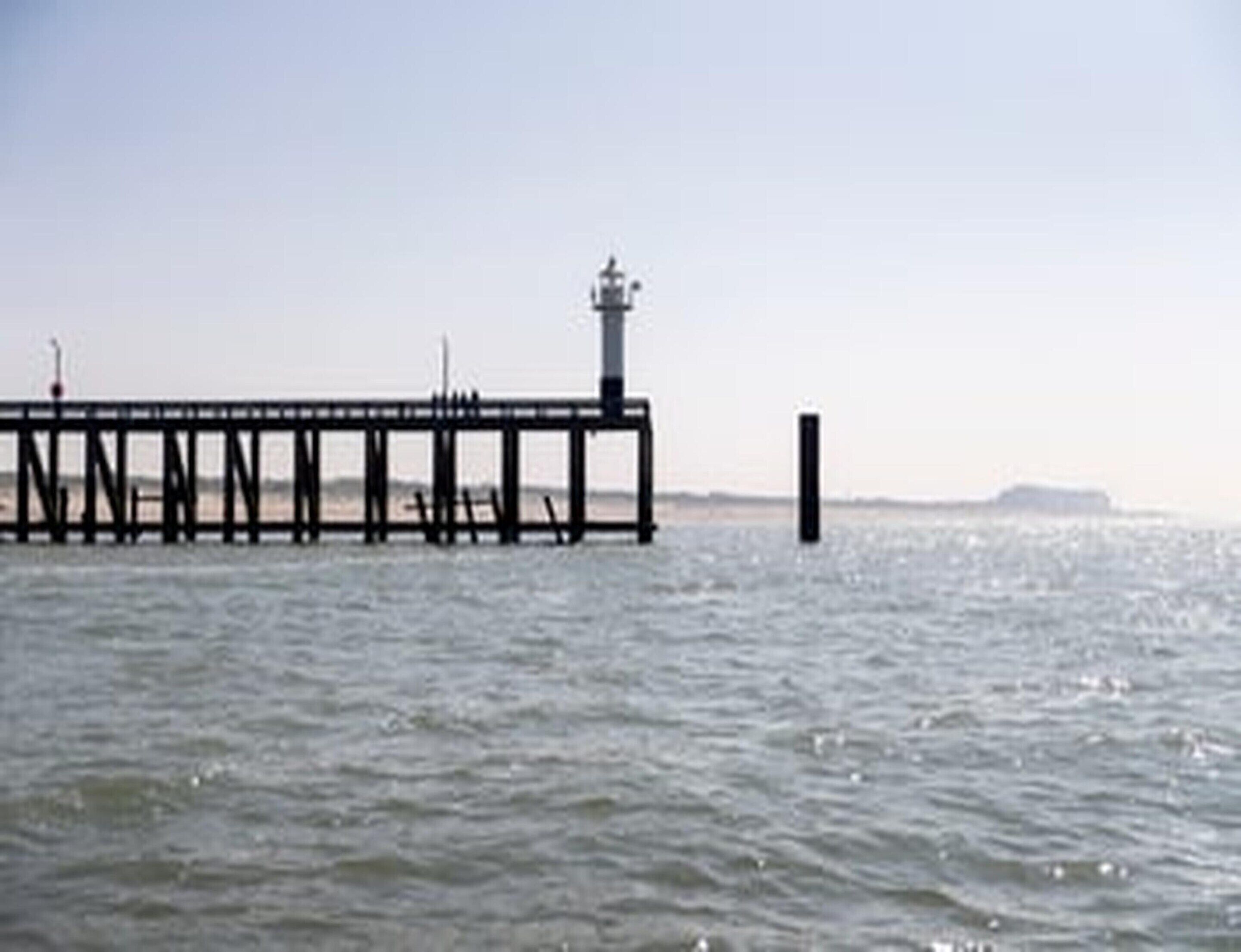 A pier extending into calm water with a clear sky above.