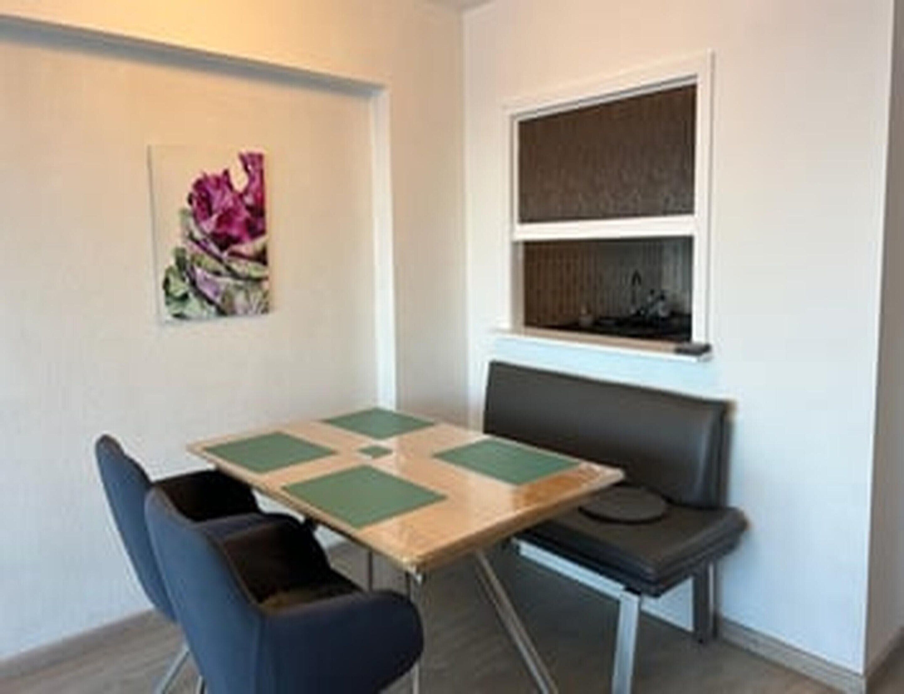 A small room with a table, two chairs, a bench, a window, and a painting on the wall.