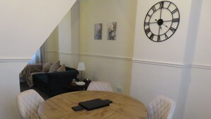 A room with a round wooden table, four chairs, a clock on the wall, a couch, and a lamp.