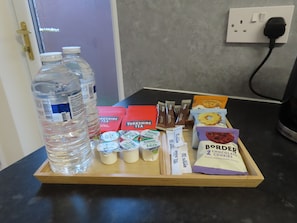 A tray with bottled water, Yorkshire Tea, milk, sugar packets, and chocolate cookies on a kitchen counter.