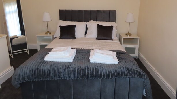 A neatly made bed with pillows, a bedside table with a lamp, a mirror, and artwork on the wall.