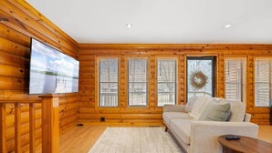 Ein Blockhaus-Interieur mit einer Couch, einem an der Wand befestigten Fernseher und einem Kamin.