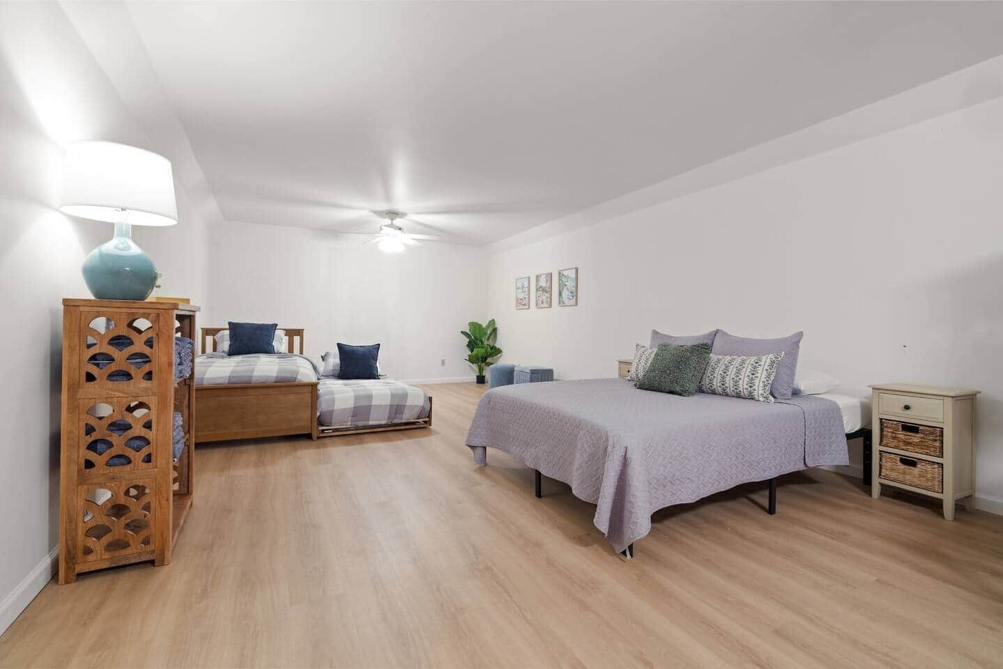 Un dormitorio con dos camas, un ventilador de techo, una mesita de noche de madera y una lámpara fijada a la pared.