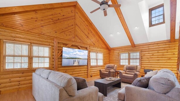 Ein rustikales Blockhaus-Interieur mit Deckenventilator, großem Fernseher und einer gemütlichen Sitzecke mit Sofas und Sesseln.