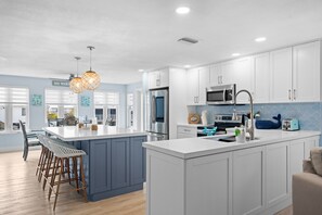 A modern kitchen with white cabinets, a large island, stainless steel appliances, and a blue accent wall. - Catch of the Bay - Waterfront - Pool - 35' Dock (Marathon)