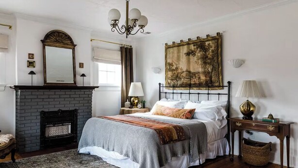 A bedroom with a fireplace, a bed with a patterned bedspread, a large painting on the wall, and a chandelier. - The Kenwick Pied-à-terre - Lexington Apartment with Historic Charm (Lexington)