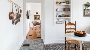 A dining area with a round table, a chair, a bowl of fruit, a white wall, a shelf with kitchen items, and a door leading to another room. - The Kenwick Pied-à-terre - Lexington Apartment with Historic Charm (Lexington)