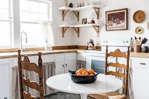 Une cuisine avec des meubles blancs, une cuisinière et une table à manger avec des chaises.