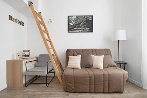 A room with a brown sofa, a wooden ladder, a desk with a chair, a lamp, and a framed picture on the wall. - Charming Air-Conditioned Studio in Cannes (Cannes)