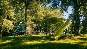 A playground with a slide and swings, surrounded by trees and grass.
