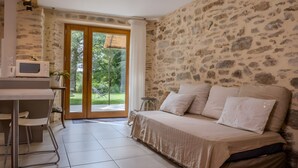 A room with a stone wall, a bed with pillows, a microwave, a chair, and a table.