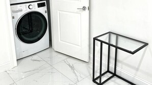 Uma lavanderia com duas máquinas de lavar empilhadas, uma porta branca e uma mesa de vidro com estrutura metálica.
