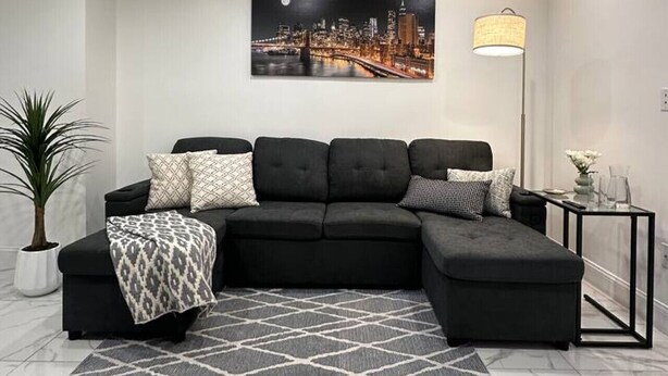 Uma sala de estar moderna com sofá em formato de L, uma pintura de paisagem urbana, abajur de chão e planta em vaso.