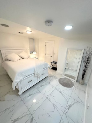 Un dormitorio con cama, mesita de noche, espejo, puerta y suelo de mármol.
