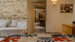 A room with a bed, a sofa, a dining area with chairs, a table, and a wall with a light fixture and a framed picture. - Gîte De La Fontaine – Entire Property, Sleeps 13, Les Cammazes (Les Cammazes)