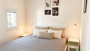 Un dormitorio con cama, dos mesitas de noche, un ventanal y cuadros colgados en la pared.