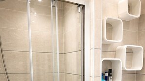 Un baño moderno con cabina de ducha de vidrio, un lavamanos redondo y estantes empotrados.