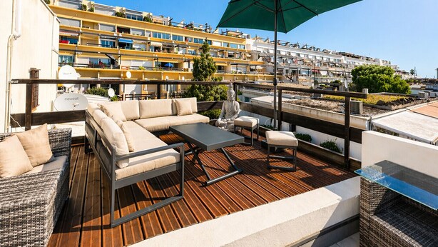 Una terraza en la azotea con un conjunto de sofás, una mesa y una sombrilla.
