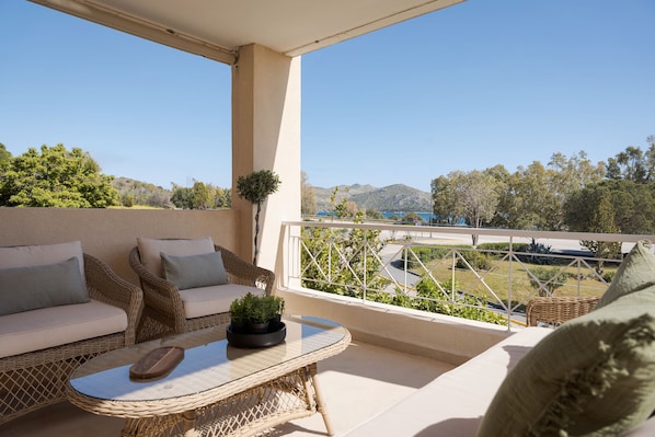 Un balcón con mobiliario de mimbre, una mesa de vidrio y vistas a un paisaje montañoso.