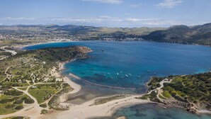 An aerial view of a coastal area with clear blue waters, a sandy beach, and a winding road. - Aegean Essence Villa (Saronikos)