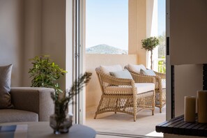 Quarto com sofá, mobiliário de vime, planta em vaso e vista para o exterior.