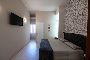 A bedroom with a bed, a flat-screen TV mounted on the wall, a patterned wall, and a door leading to another room. - Suite Ionio - Teresita Guest House (Gallipoli)