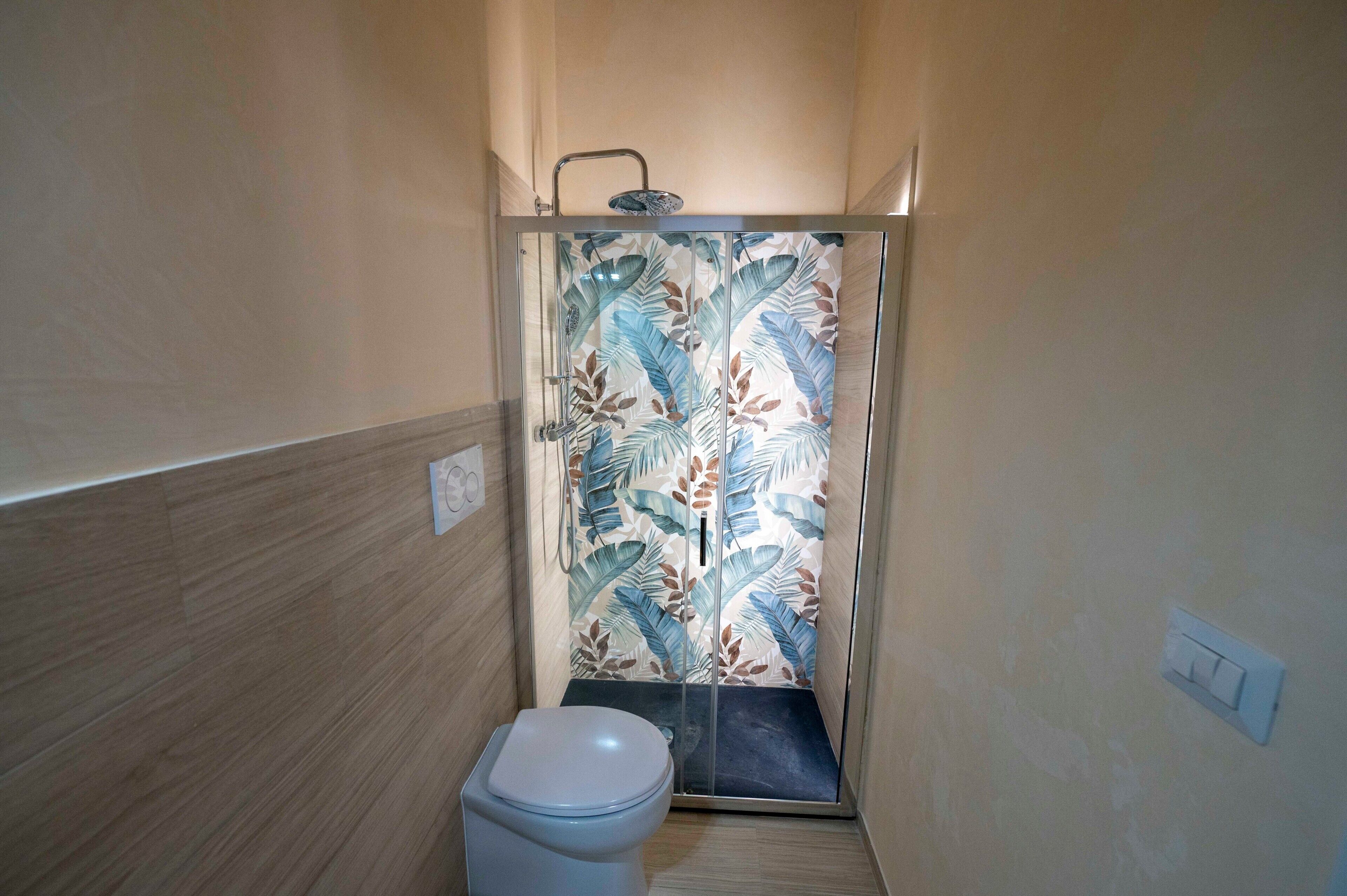 Et badeværelse med bruser, toilet og en væg med blomstermønster.