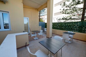 A covered outdoor seating area with tables and chairs, a window, and a hedge. - Suite degli Ulivi - Teresita Guest House (Gallipoli)