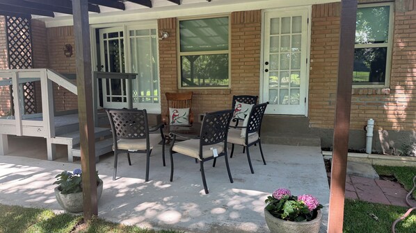 Un patio cubierto con fachada de ladrillo, una mesa y sillas de madera y una planta en maceta.
