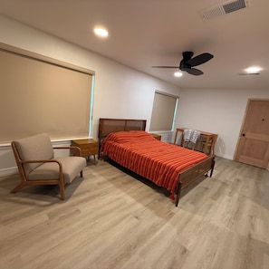 A bedroom with a bed, a chair, a desk, a ceiling fan, and a window.