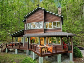 Une cabane en bois à deux étages, dotée d’une terrasse, de grandes fenêtres et d’une cheminée.