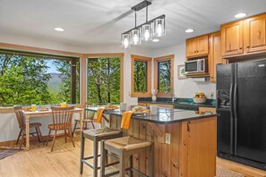Una cocina con armarios de madera, un refrigerador negro, un microondas y un comedor con sillas y una mesa.