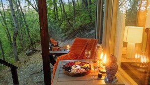 Une terrasse en bois avec une table dressée pour un repas, une sculpture d’oiseau décorative et une vue sur une zone boisée.