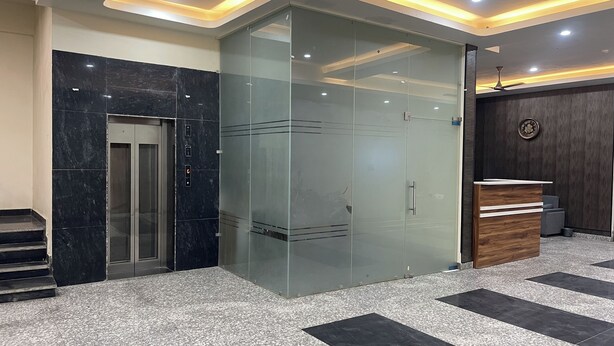 Un espace d’accueil doté d’une cloison en verre, d’un comptoir de réception et d’un escalier menant à un ascenseur.