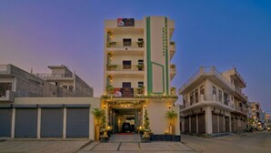 Un hôtel à plusieurs étages doté de balcons, une enseigne indiquant qu’il s’agit d’un hôtel, et une vue sur la rue avec d’autres bâtiments.