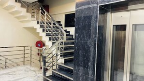 Un escalier avec des rampes en métal, un extincteur et une porte d’ascenseur en verre.