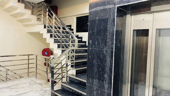 Un escalier avec des rampes en métal, un extincteur et une porte d’ascenseur en verre.