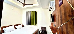 A hotel room with a bed, a ceiling fan, a TV, and a wooden wardrobe.